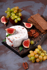 Fresh homemade cheese with dried tomato, fenugreek and herbs served on wooden board with fig, grape, pecan nuts and crispbread
