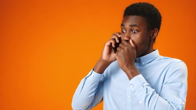 Worried young african man talking on the phone recieving bad news against orange background