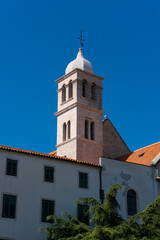 Fototapeta na wymiar church tower (steeple) in the middle of an old town with a blue sky in Sibenik, Croatia