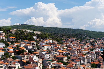 view of the city Sibenik, Croatia with traditionel houses (with red/orange roofs), a hill and a forest