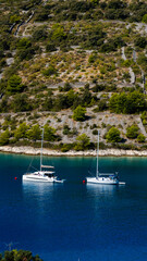2 sail boats (1 catamarans) in a bay with olive trees in the background in Sevid, Croatia