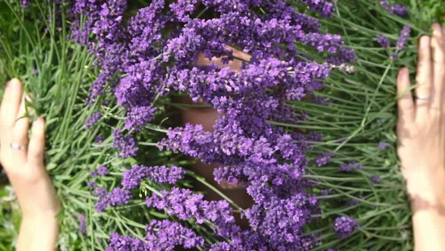 No-makeup woman enjoying sunshine lying among lavander flowers in blossom field and feeling the connection with nature. Self care, mind body and soul.