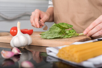 Women's hands cut basil on the kitchen table.