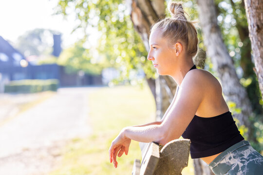 Young smiling female resting after an active fitness training while leaning over a wooden fence or bench, satisfied fit woman resting after an active fitness training. High quality photo
