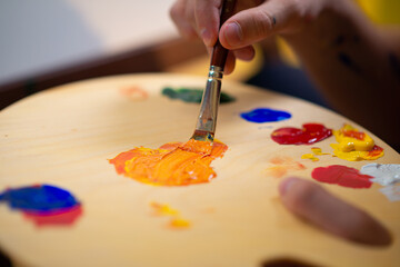 A man is using a flat brush to mix two colours on a palette and paint onto a canvas