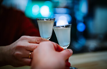 Two hands clinking shots of alcoholic beverage in bar