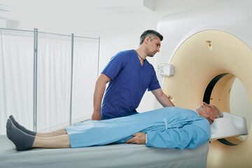 Computed Tomography. Male medical worker helping senior patient during CT scan procedure, talking...