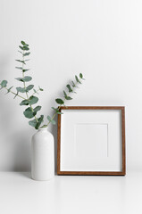 Square wooden frame mockup with eucalyptus twig in white room with copy space for artwork