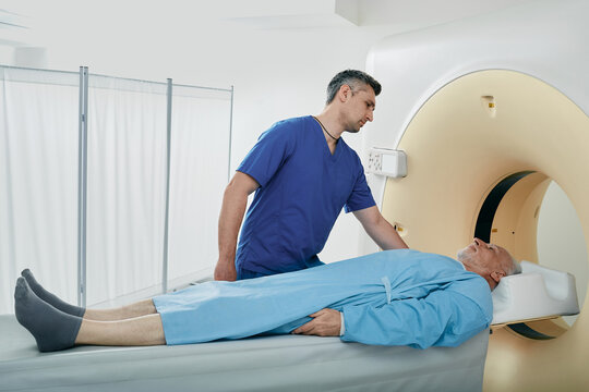 Computed Tomography. Male medical worker helping senior patient during CT scan procedure, talking with him in hospital radiology department