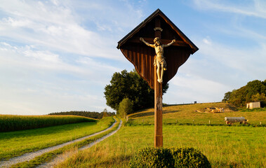 a footpath in the fields and a wooden cross with Jesus Christ in the Bavarian village Konradshofen...