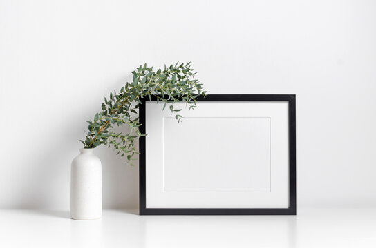 Blank horizontal frame mockup in white minimalistic interior with green plant decor