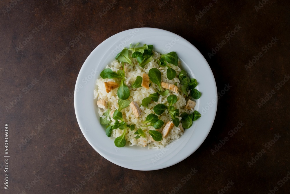 Wall mural chicken and rice with valeriana salad on a plate on a wooden table