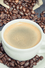 White cup of coffee and roasted fragrant dark coffee grains in bag