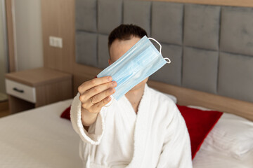 Man in bathrobe holds medical mask. Safety tourism. Virus protection on trips