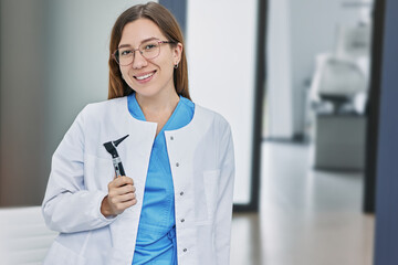Portrait of female audiologist with otoscope standing in hearing clinic - obrazy, fototapety, plakaty