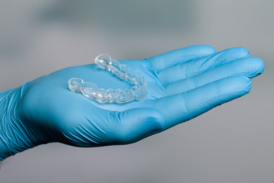 Dentist hand in blue gloves presenting a transparent removable aligner in front of dentistry room