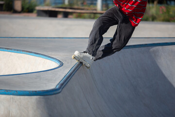 Inline skater doing trick in outdoor skatepark. In-line roller blader performing top acid grind on rail in concrete mini ramp - obrazy, fototapety, plakaty
