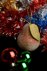Pear. Fur-tree toy with balls and tinsel on a black background.