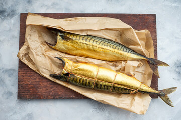 two smoked mackerel fish on a wooden board with parchment on a light background
