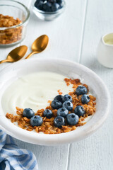 Yogurt. Greek Yogurt with granola and fresh blueberries in white bowl over old white wood background. Morning breakfast concept. Healthy food for breakfast, top view