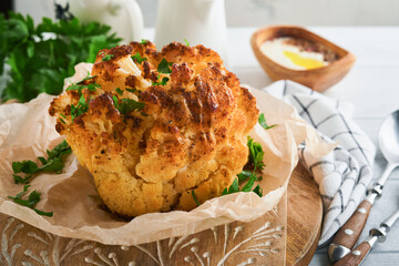 Baked cauliflower. Oven or whole baked cauliflower spices and herbs server on wooden rustic board on old white wooden background table. Delicious cauliflower. Eyal Shani dish. Perfect tasty snack.