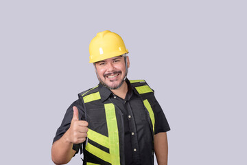 A burly foreman or engineer wearing a hardhat and safety vest gives a thumbs up of approval. Isolated on a gray background.