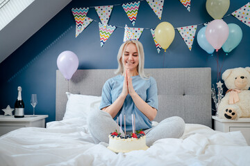 Happy emotional woman in pajama and party cap after blowing out the candles on birthday cake,...