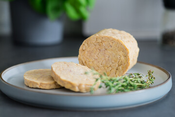 Raw Tempeh or Tempe, made of fermented soybean seeds on kitchen table. Tempeh Slices on plate with herbs. Soya protein. Plant based meat concept. Healthy eating. Go vegan. Selective focus, copy space