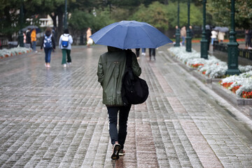 Rain in city, girl in raincoat walk with umbrella on a street on people background. Rainy weather in autumn