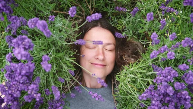 Natural beauty. Portrait of woman without makeup lying among lavander flowers in blossom field. Happy smiling female relax on the grass on sunny summer day feeling connection with nature.