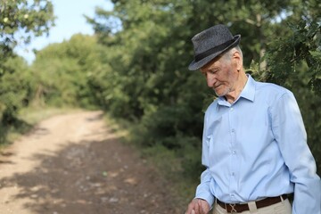 Caucasian old male on the side of a dirt road in a countryside