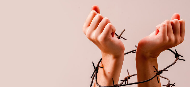 Child's fragile hands tied with barbed wire as symbol of fighting for freedom and human right. Horizontal image with copy space for text or design.