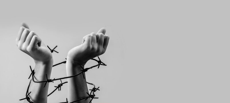Child's fragile hands tied with barbed wire as symbol of fighting for freedom and human right. Black and white image. Copy space for text or design.