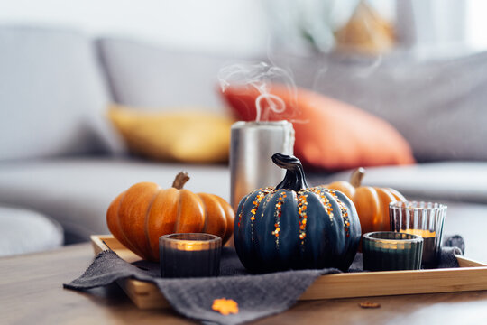 Autumn cozy composition for hygge home decor. Orange and gray pumpkins, just blown out candles with smoke on a tray with a gray napkin on a coffee table in the living room. Selective focus. copy space