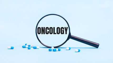 On a blue background, white and blue capsules with pills and a black magnifying glass with the text ONCOLOGY. Medical concept.