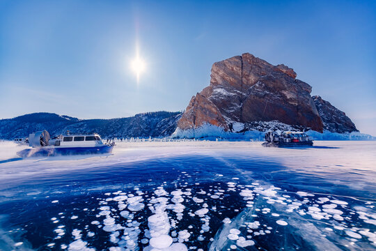 Winter landscape sunny day blue clear ice on Baikal lake with hovercraft