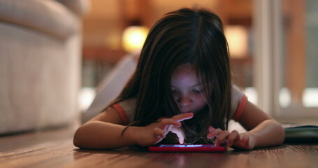 Little girl using cellphone device at night at home. Child staring at smartphone screen