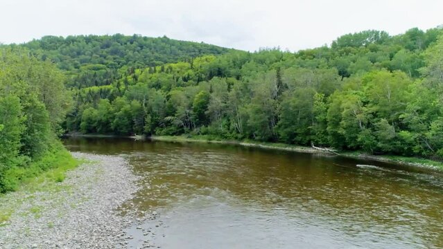 Aerial drone footage flying at low altitude over the Matane river in the summer.