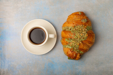 Aromatic coffee in a cup with pistachio croissant on a textural background.Espresso. Morning drink. Breakfast. Cheerful morning concept. Place for text. Place to copy.