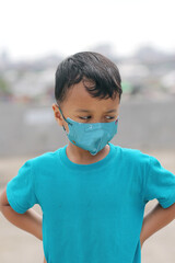 a boy wearing a blue shirt and mask looking down sharply the background is intentionally blurred and selective focus