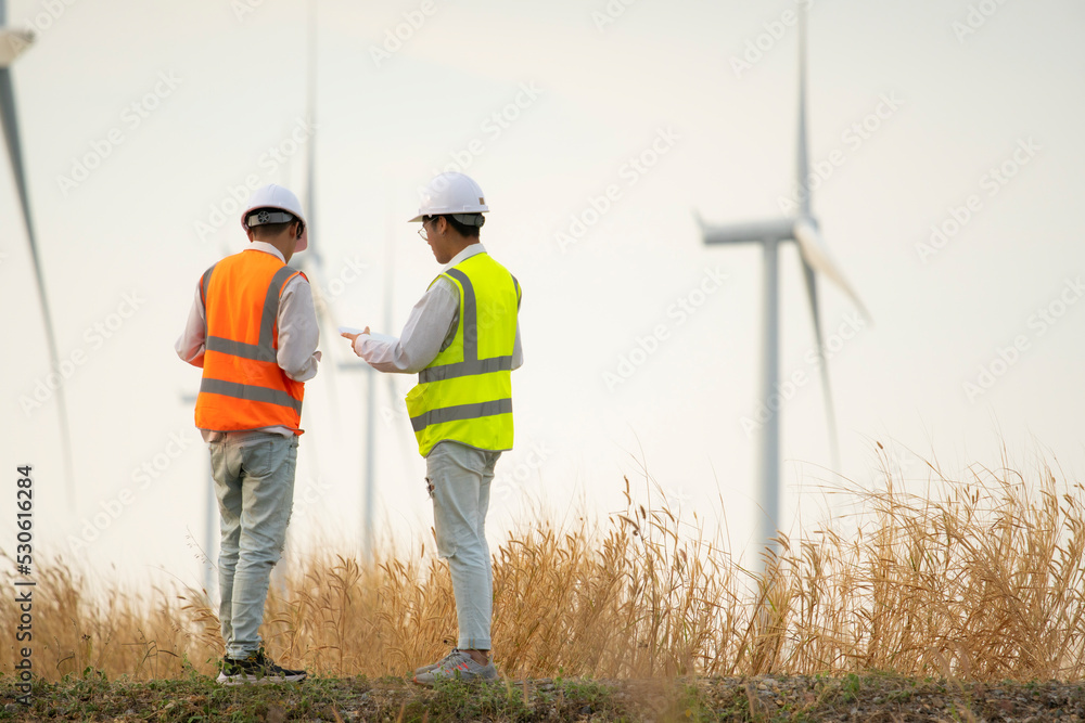 Wall mural two asian engineers or technician men in uniform discuss and checking. wind turbines ecological ener