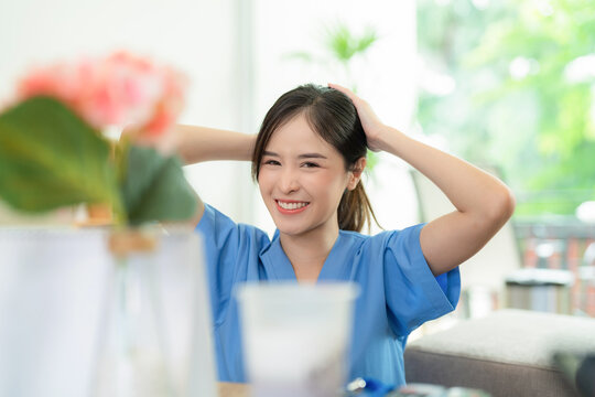 Young Asia Pretty Doctor Sitting At Nursing Home With Smile And Collect Hair Before Work. Medical Health Care Worker In Blue Uniform Work At Clinic Or Hospital. Business And Medical Healthcare