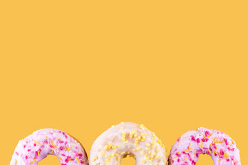 pink and yellow spricled  donuts on a yellow background Space for text high-quality photos for calendar and cards