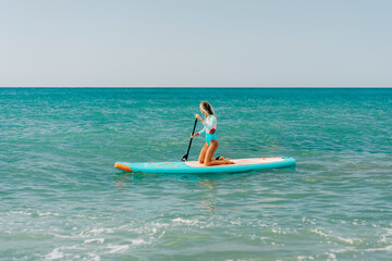 A young athletic woman is paddling on a paddleboard on the sea.