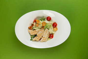 Salad with chicken and tomato in a plate on a green background.