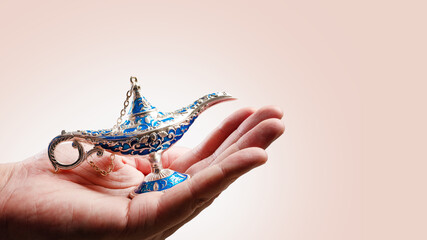 Antique magic lamp of Aladdin in a female hand on a white background. Minimalism. Close-up. Arabian tales, oriental myths. Symbol of wealth, good luck. Advertising, banner.
