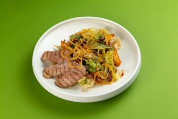Salad with pieces of duck in a plate on a green background.