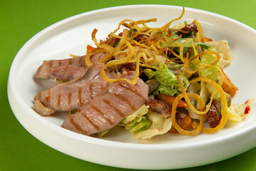 Salad with pieces of duck in a plate on a green background.