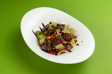 Salad with fried liver in a plate on a green background.