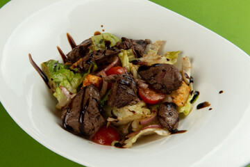 Salad with fried liver in a plate on a green background.